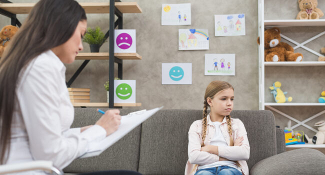 depressed-girl-sitting-sofa-with-female-psychologist-writing-note-clipboard