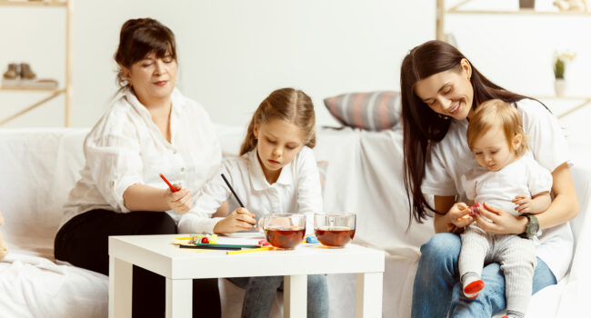 Two little girls their attractive young mother and their charming grandmother sitting on sofa and spending time together at home. Generation of women. International Women's Day. Happy Mother's Day.